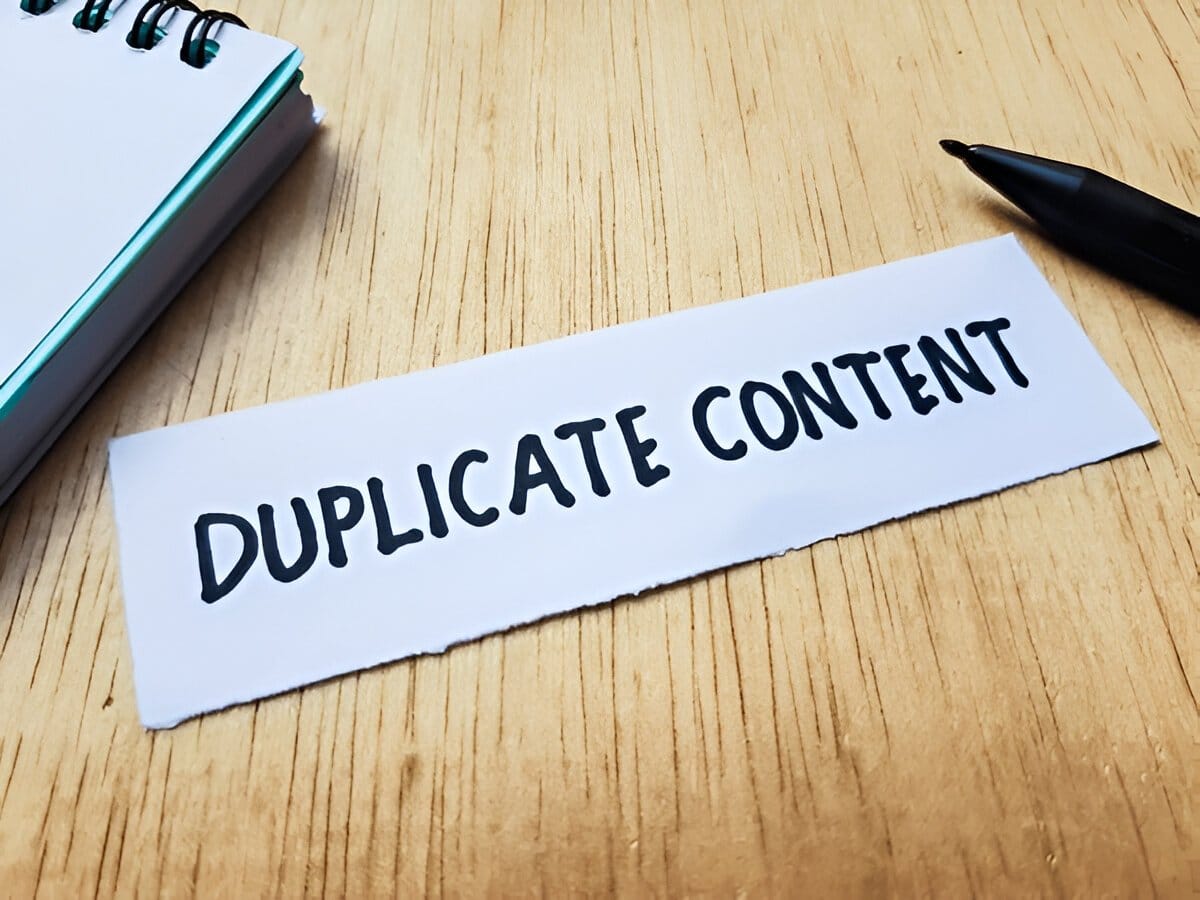 Duplicate Content text written on paper placed on a wooden desk with a notebook and pen.